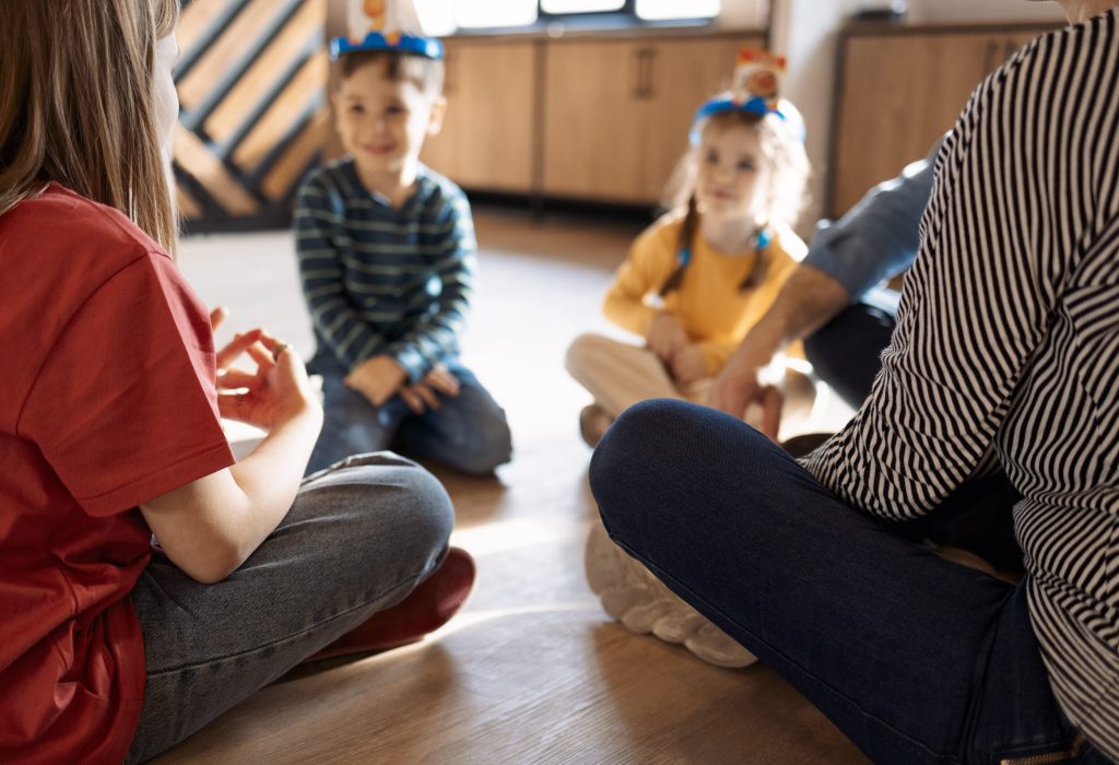 Happy young family with kids playing a card game at home sitting on the floor. Mother, father, son and daughters playing card games in a living room